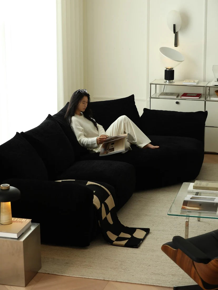 Woman reading a magazine on a black sofa in a modern living room.