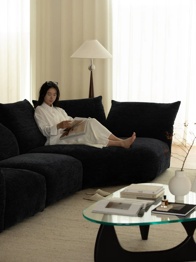 Woman sitting on a dark gray sectional sofa in a modern living room.