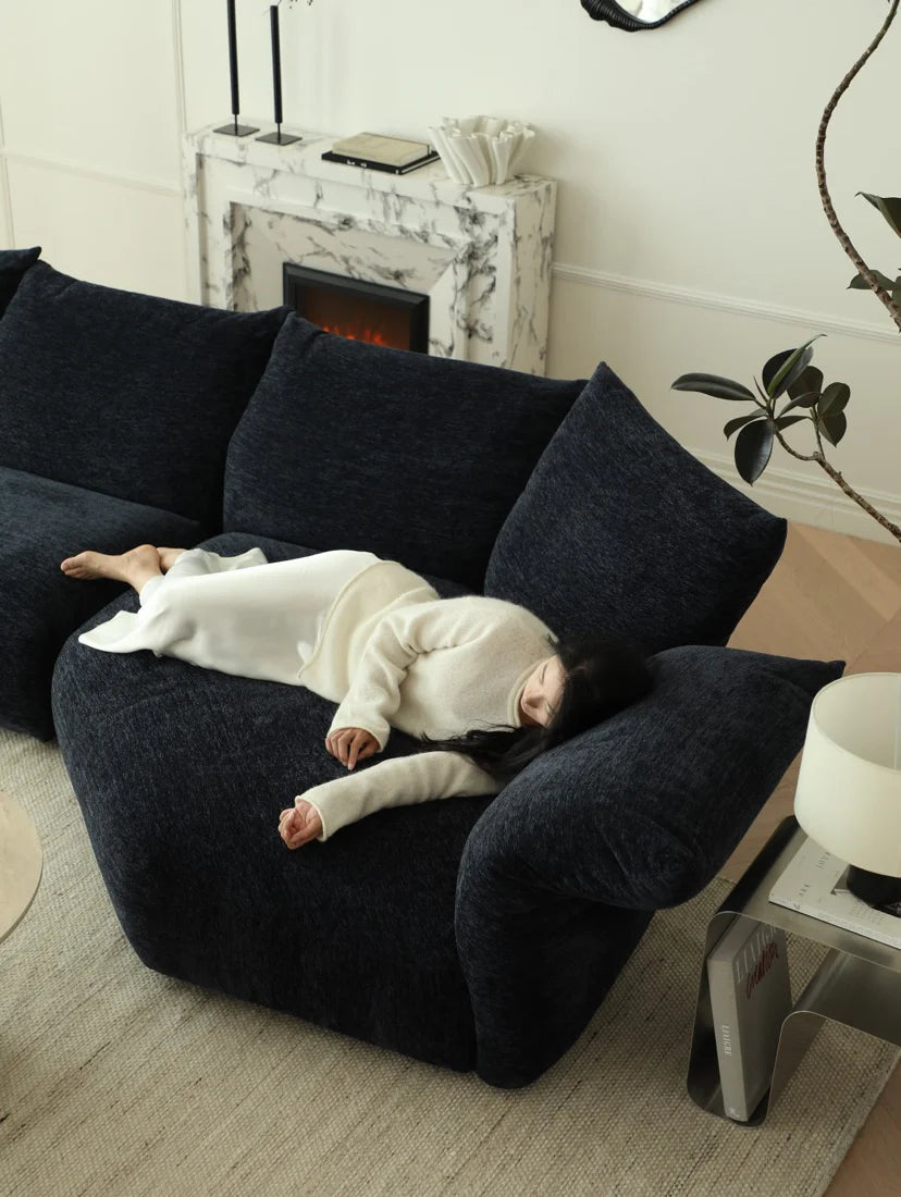 Child lying on a dark blue cushioned chair in a living room with a fireplace and decor.
