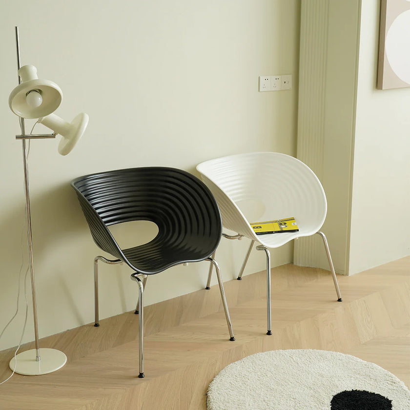 Two chairs, one black and one white, in a room with a floor lamp and light-colored walls.