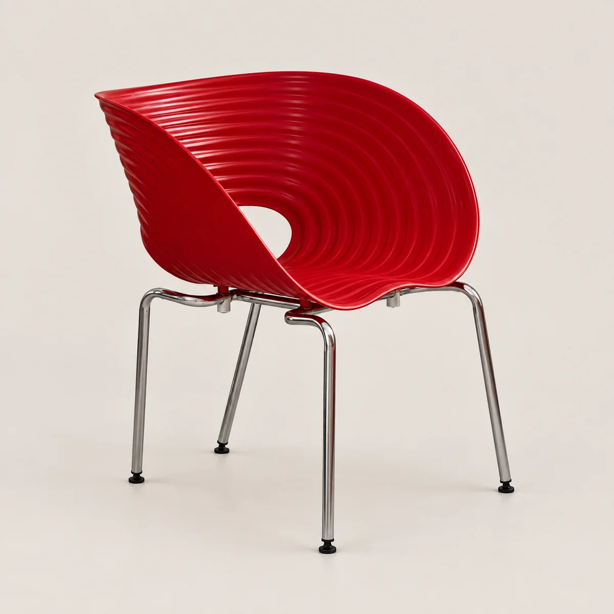 A modern red molded plastic chair with a ribbed shell back and seat, supported by four slim chrome metal legs, shown against a light beige studio background.