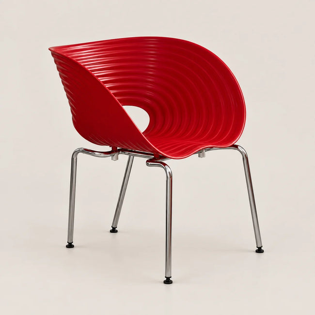 A modern red molded plastic chair with a ribbed shell back and seat, supported by four slim chrome metal legs, shown against a light beige studio background.